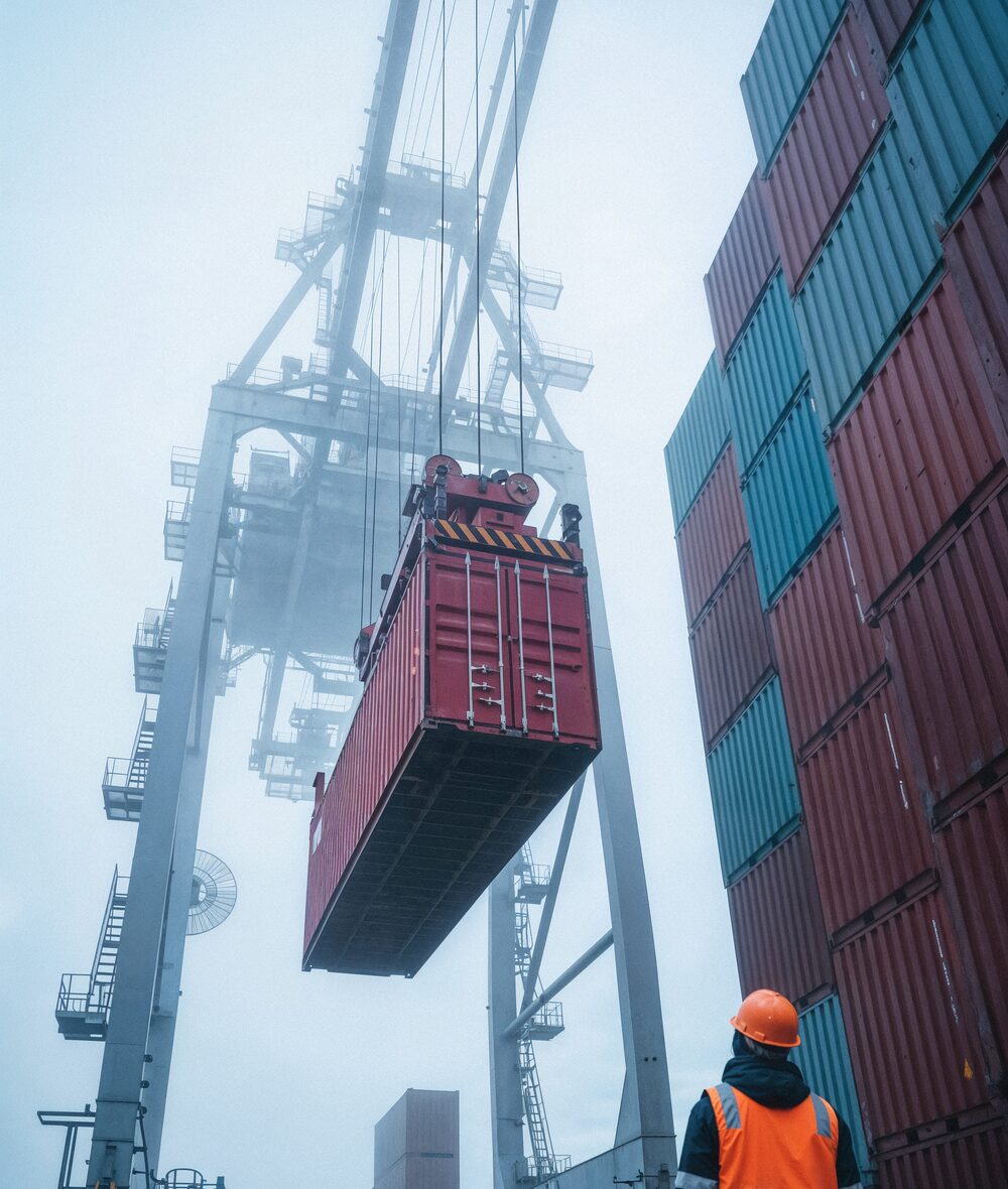 Port crane lowering a shipping container while a dockworker looks on
