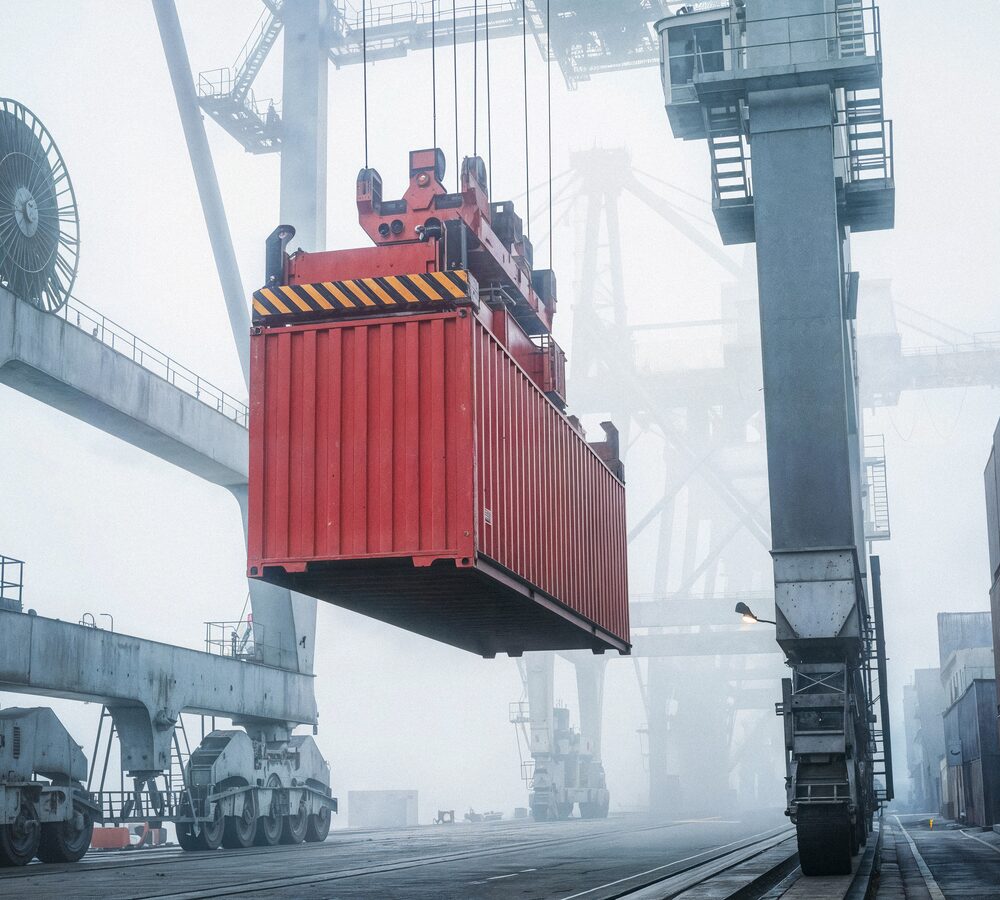 Crane lowering a red shipping container onto a rail car in foggy conditions
